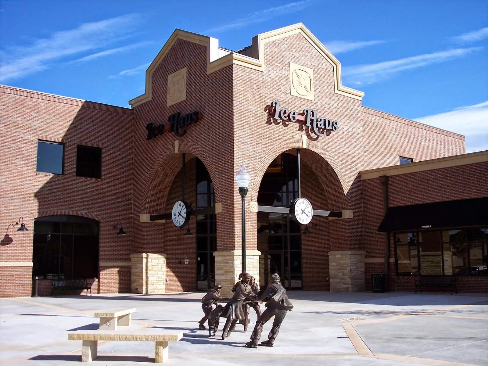 Frente de ladrillo de Greeley Ice Haus con dos entradas en arco, relojes y letreros de "Ice Haus" sobre cada arco, con una escultura de bronce de niños patinando en la plaza del frente. — Greeley Ice Haus