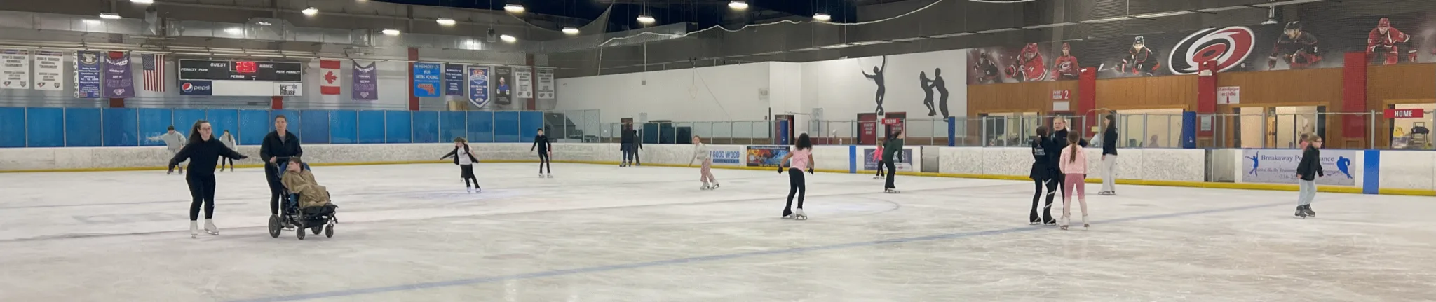 Wide panorama of the full sheet during a public skate, with Carolina Hurricanes murals on the far wall — The Greensboro Ice House