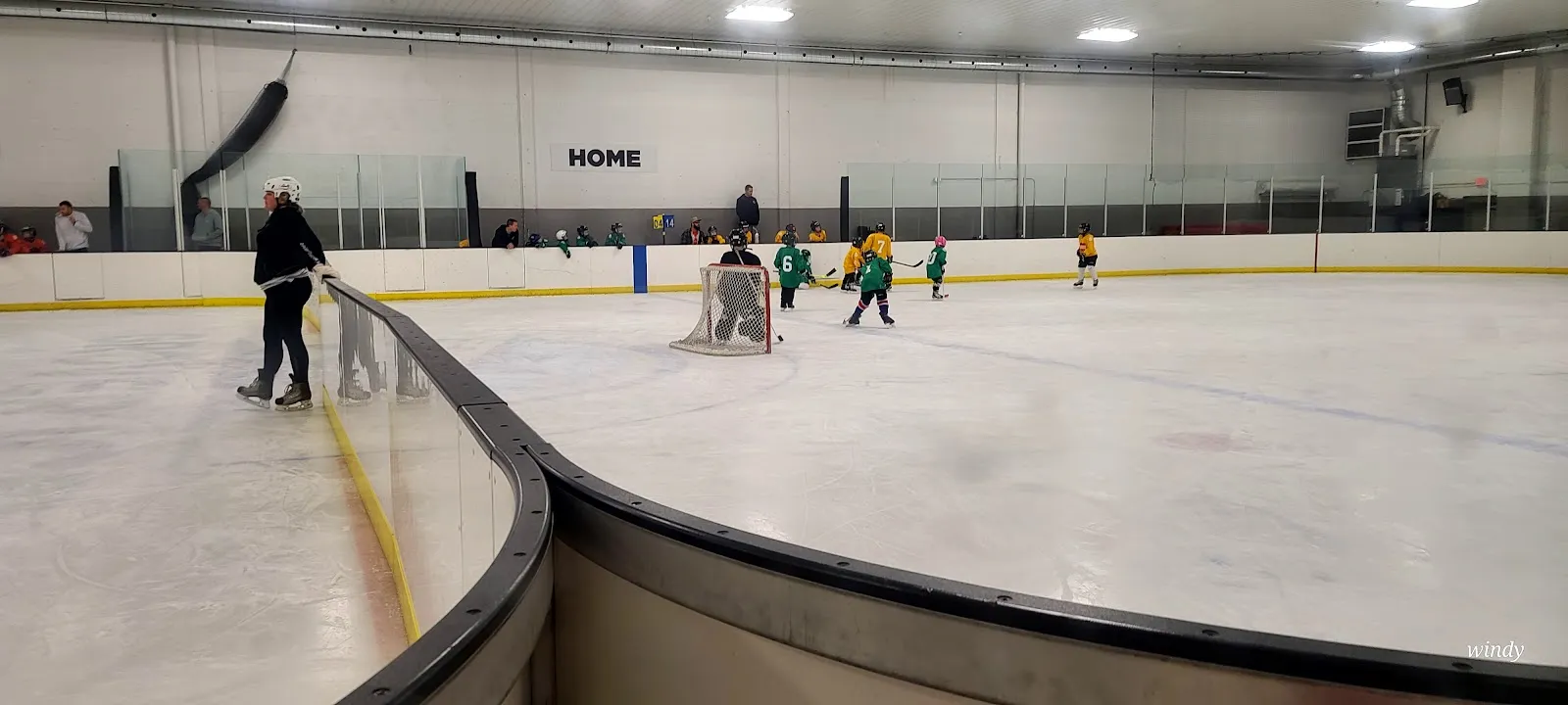 A youth hockey session on the Grover Ice Rink sheet, seen along the curved boards toward the far net. — Grover Ice