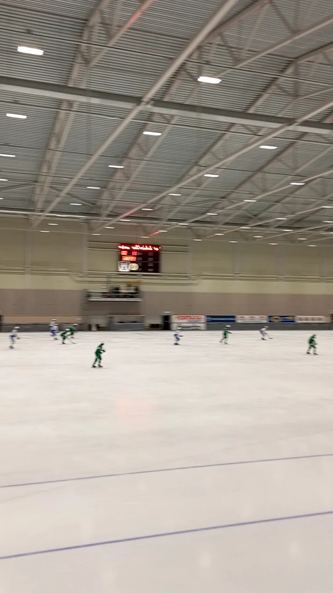 Isen i Gubbängens skridsko- och bandyhall under ståltaket, med resultattavlan – Gubbängens skridsko- och bandyhall