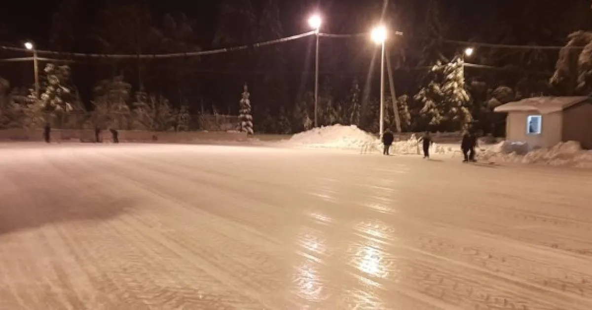 Night view of the Haapaniemi skating rink in Uusikaupunki: a smooth ice surface lit by lamp posts, with a few skaters in the distance and a small hut at the edge. — Haapaniemen luistelukenttä