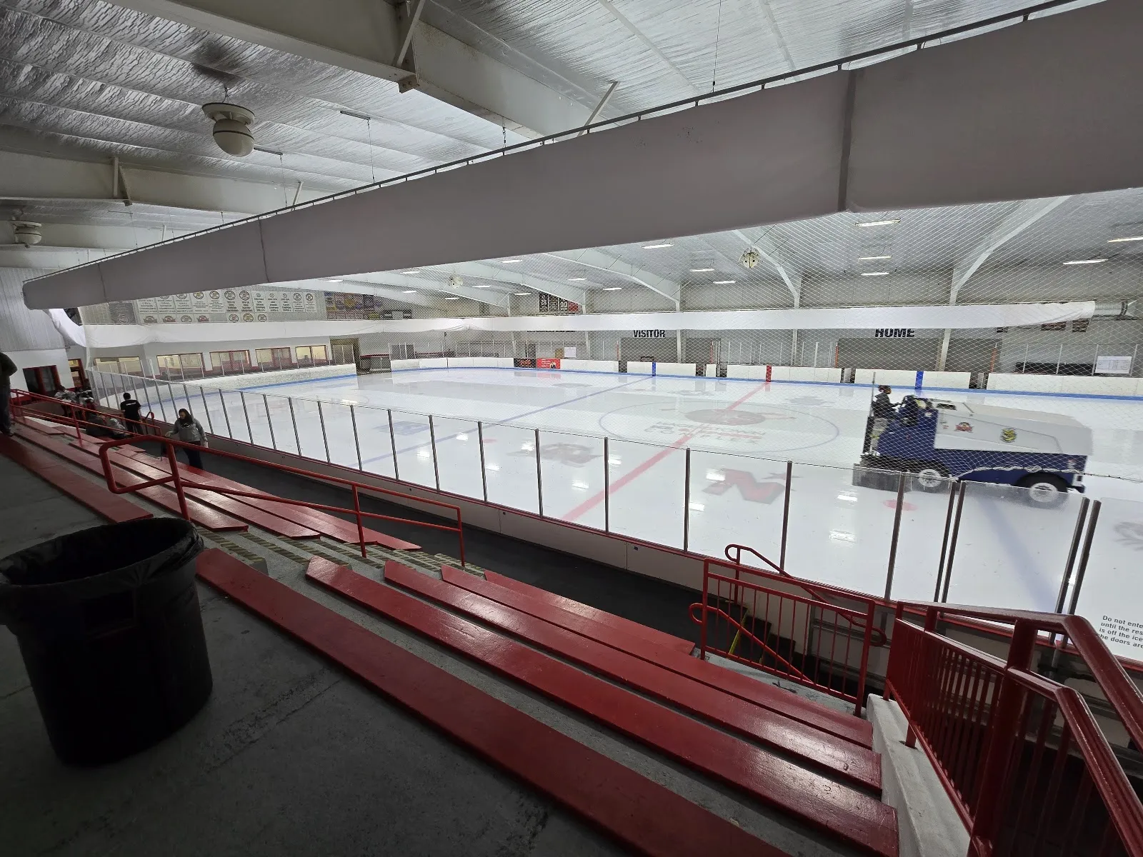 Toda la pista desde las gradas rojas durante una pasada de pulido de la Zamboni, con letreros de las bancas 'VISITOR'/'HOME' y el logotipo de la instalación en el círculo central del hielo. — Hagerstown Ice and Sports Complex