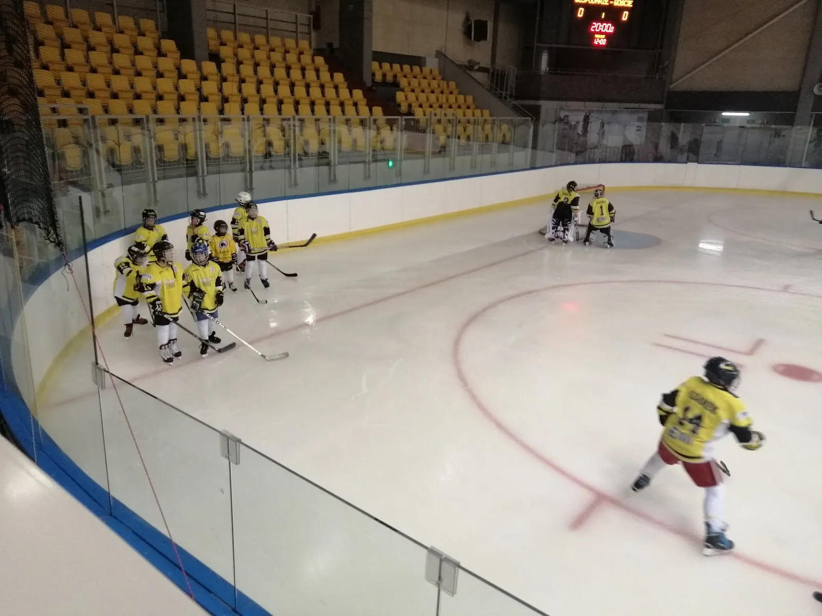 Mecz na lodzie w Hali Widowiskowo-Sportowej w Cieszynie, z zawodnikami przy bandzie i żółtymi siedzeniami trybuny za nimi. — Hala Widowiskowo-Sportowa Cieszyn
