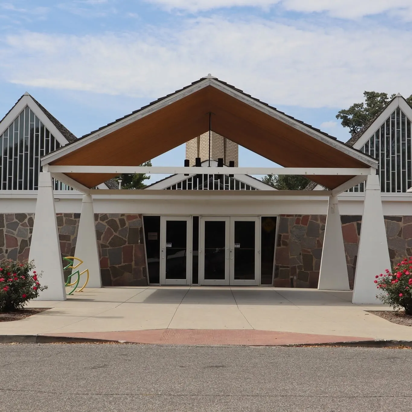 La entrada principal del edificio: una fachada de piedra con un pórtico puntiagudo de madera y blanco sobre puertas dobles de vidrio, flanqueado por dos secciones de ventanas a dos aguas — Hamilton Center Ice Arena