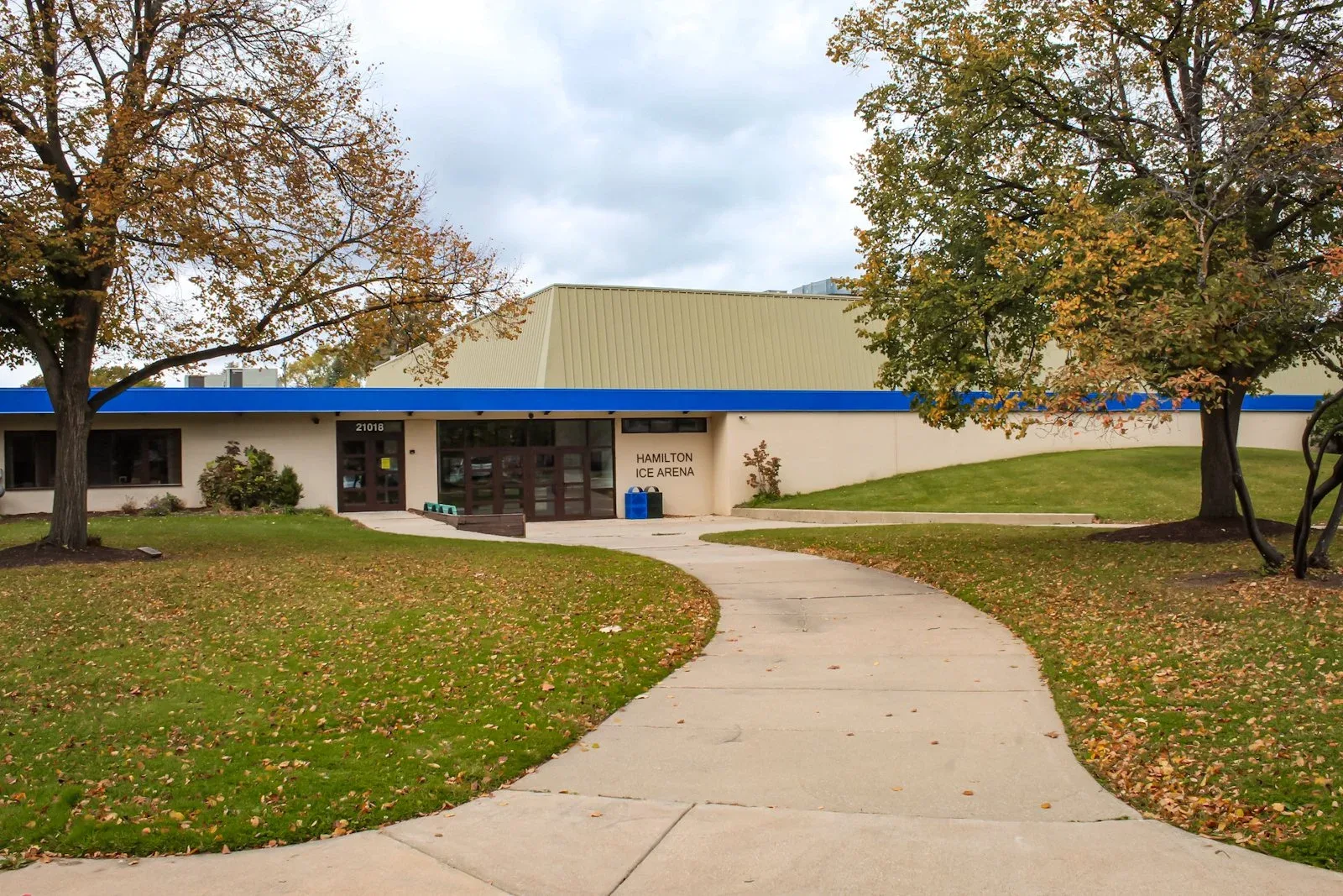 Long low tan-and-blue arena seen from the front lawn on an overcast autumn day — Hamilton Ice Arena (Rocky River)