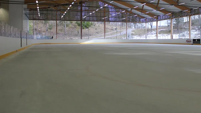The ice surface of the Hammarens ishall in Mariefred seen from the side of the open hall, with trees visible beyond the roof edge. — Hammarens ishall