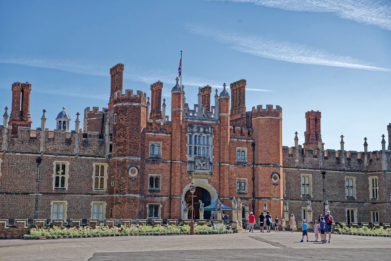 Hampton Court Palace's Tudor west front and Great Gatehouse in red brick under a blue sky; the winter rink is set up in front of the palace. — Hampton Court Palace Ice Rink