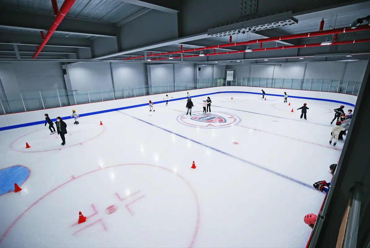 The ice of Hanam ICEBOX from the viewing gallery: a wide view across the hockey-size rink with blue boards, faceoff circles and a few skaters among cones. — Hanam ICEBOX Ice Rink