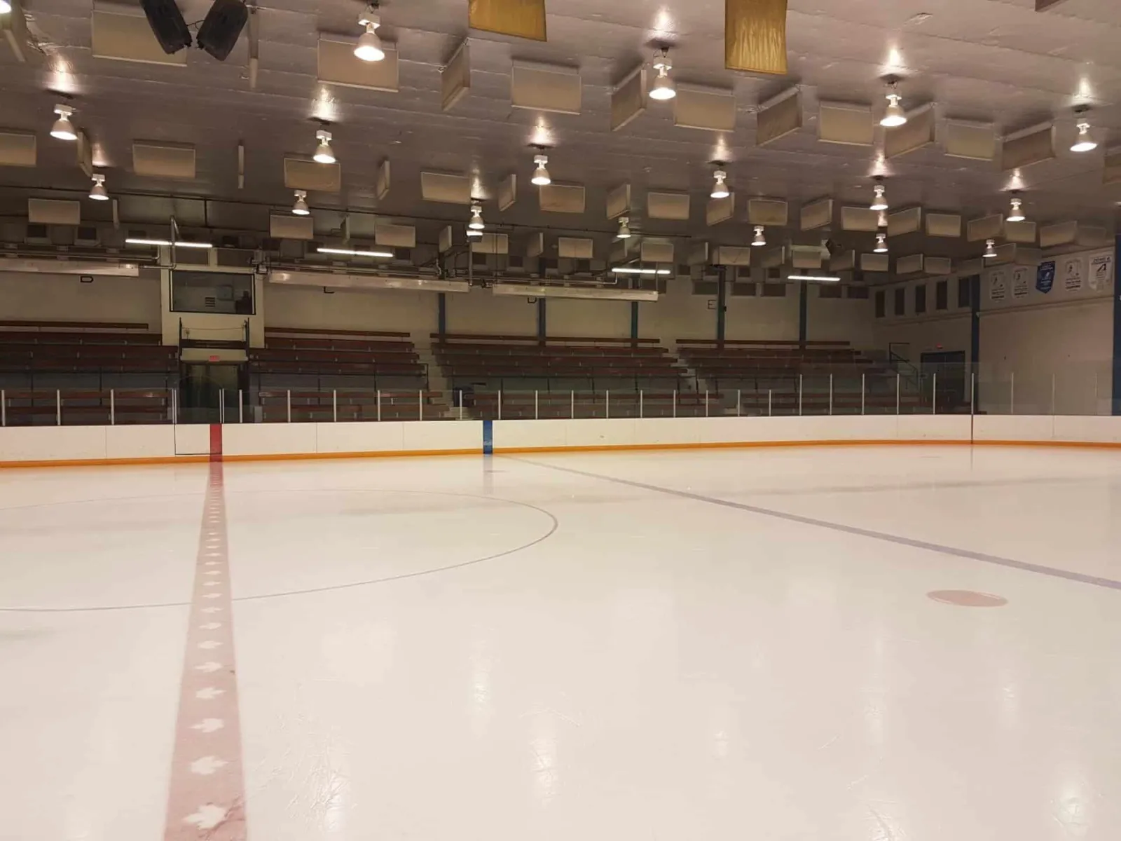 The empty regulation ice at the Hanna Arena seen along the centre line, with the bleachers on both sides. — Hanna Arena