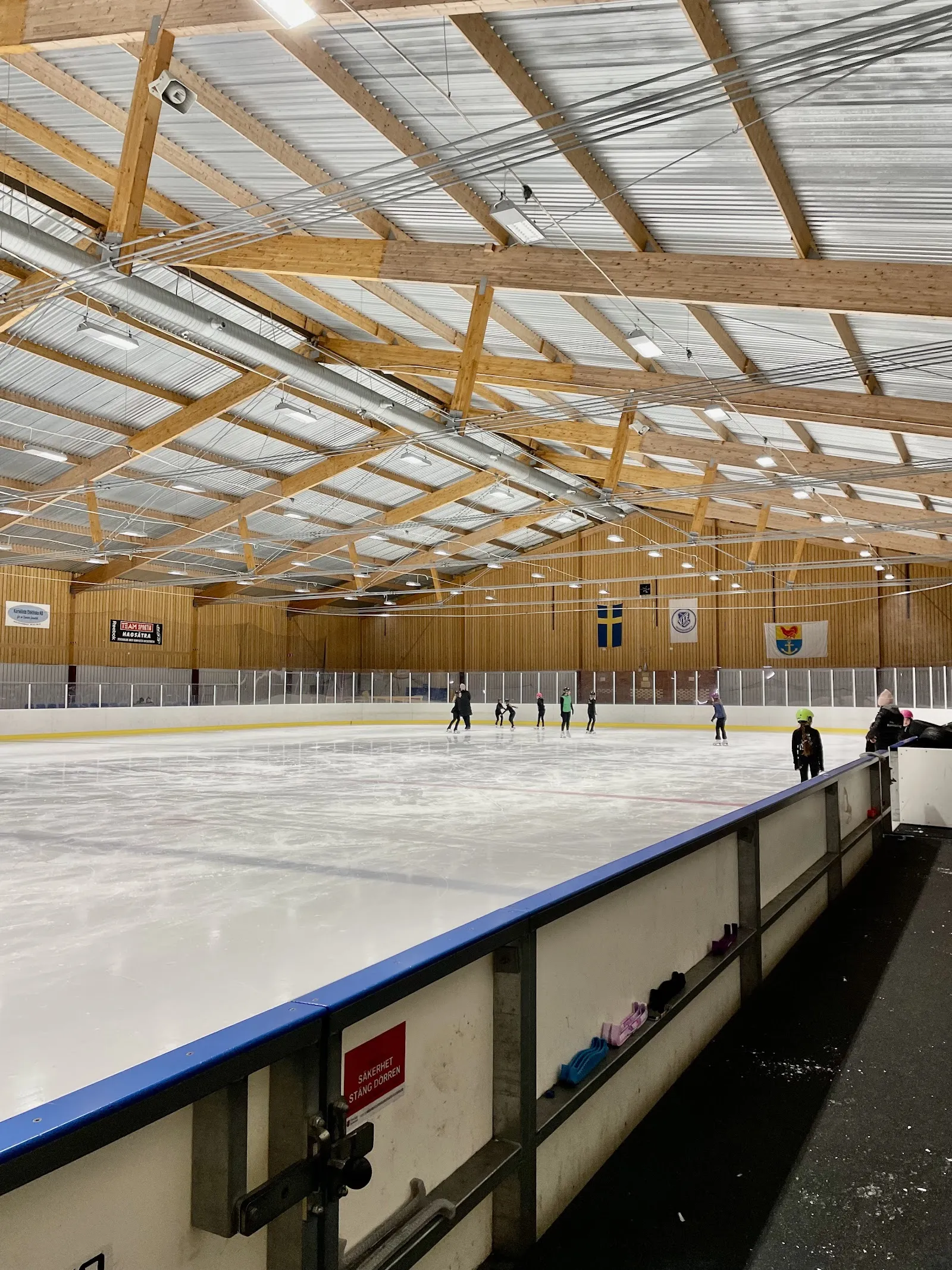 Åkare på isen i Hanvedens ishall vid sargen, under taket av limträ – Hanvedens ishall
