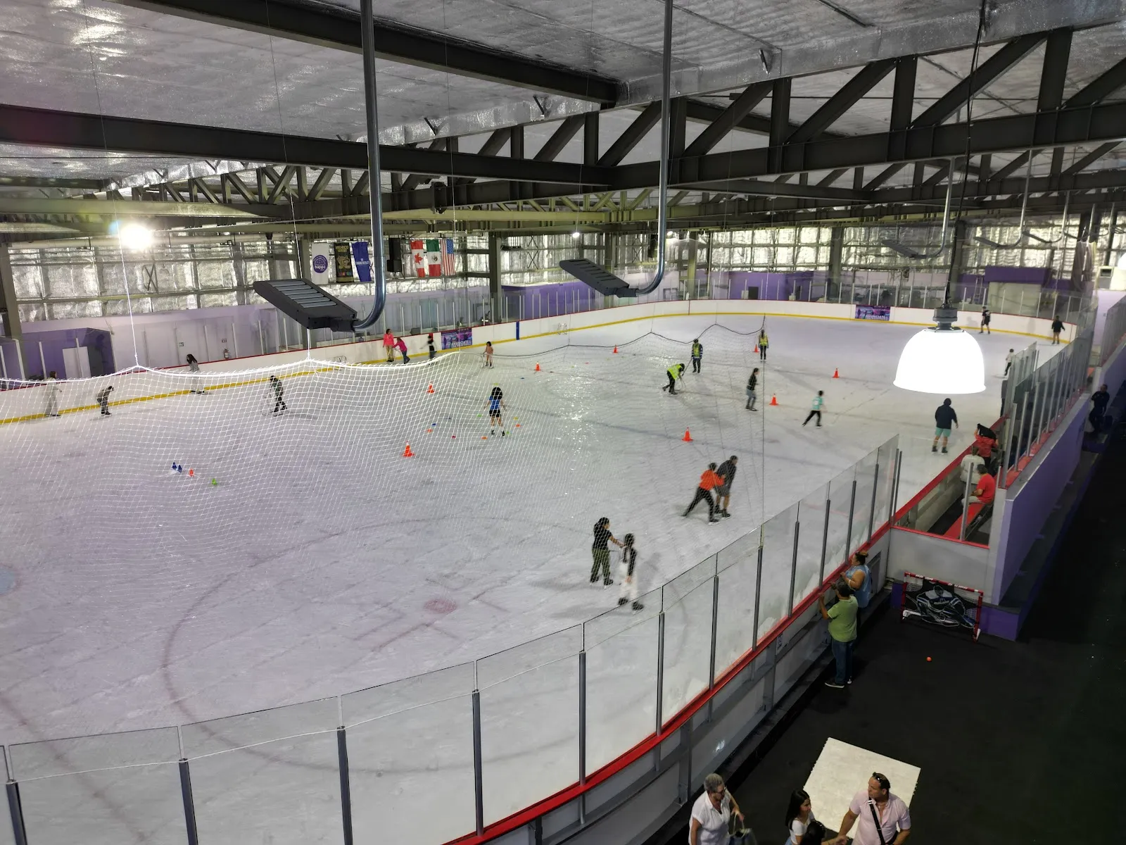 Elevated view over the indoor ice pad with public skaters and training cones spread across the ice. — Happi Arena