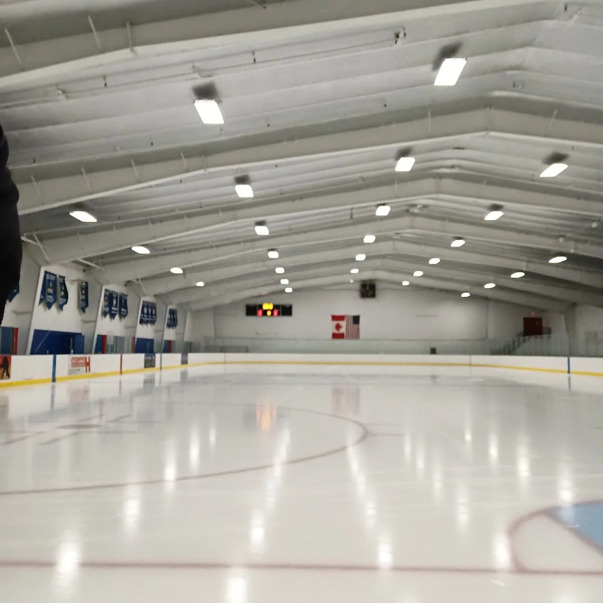 The empty sheet under a white ceiling, with championship banners along one wall and the scoreboard and flags at the far end. — Harding Arena