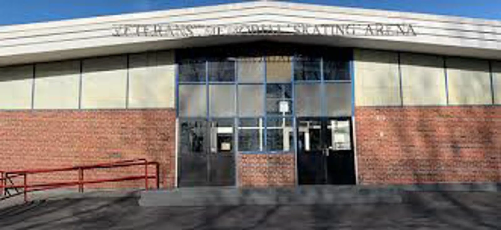 Entrada principal del edificio de la pista con las letras 'Veterans Memorial Skating Arena' a lo largo de la orilla del techo sobre la entrada de puertas dobles de vidrio, y el barandal rojo de la rampa de accesibilidad a la izquierda. — Haverhill Veterans Memorial Rink