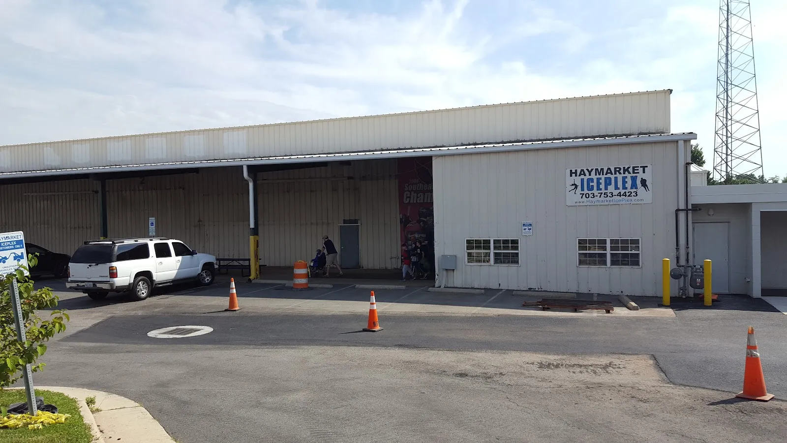 El costado del edificio con revestimiento metálico de Haymarket Iceplex, con su nombre y número de teléfono en el muro, visto desde el estacionamiento — Haymarket Iceplex