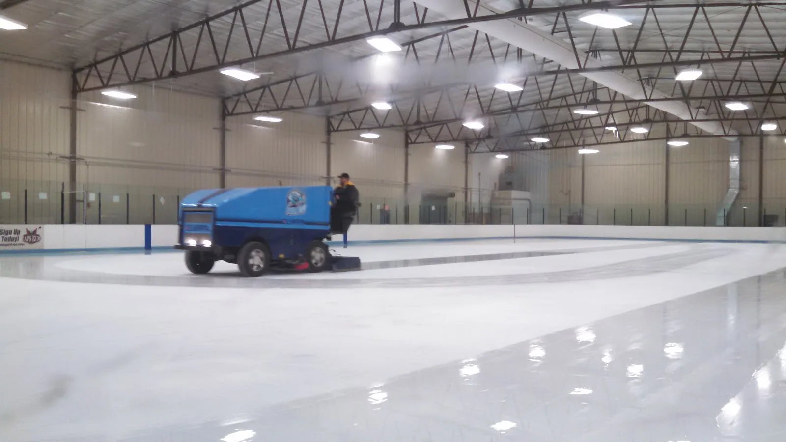 Hielo recién pulido en Haymarket Iceplex con la pulidora sobre la pista, bajo las armaduras de acero del techo — Haymarket Iceplex
