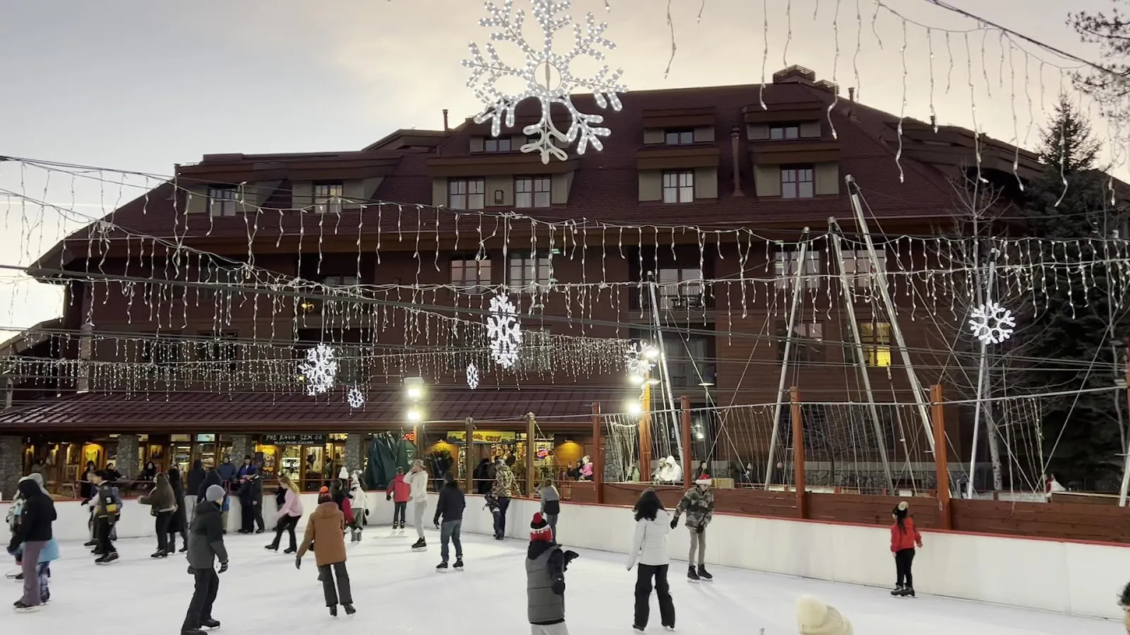 Skaters across the Heavenly Village rink in daylight with the village lodge buildings and holiday garlands behind. — Heavenly Village Ice Rink
