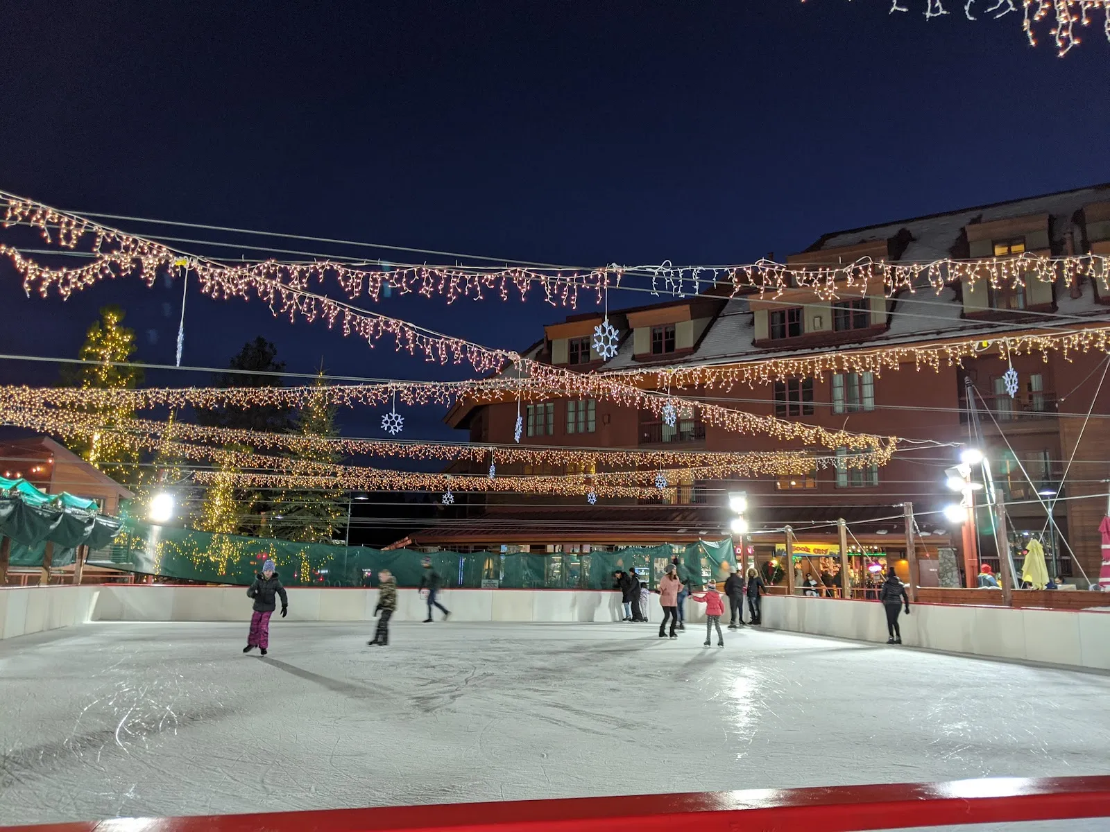 The Heavenly Village rink at dusk lit under strings of lights with skaters in the distance. — Heavenly Village Ice Rink
