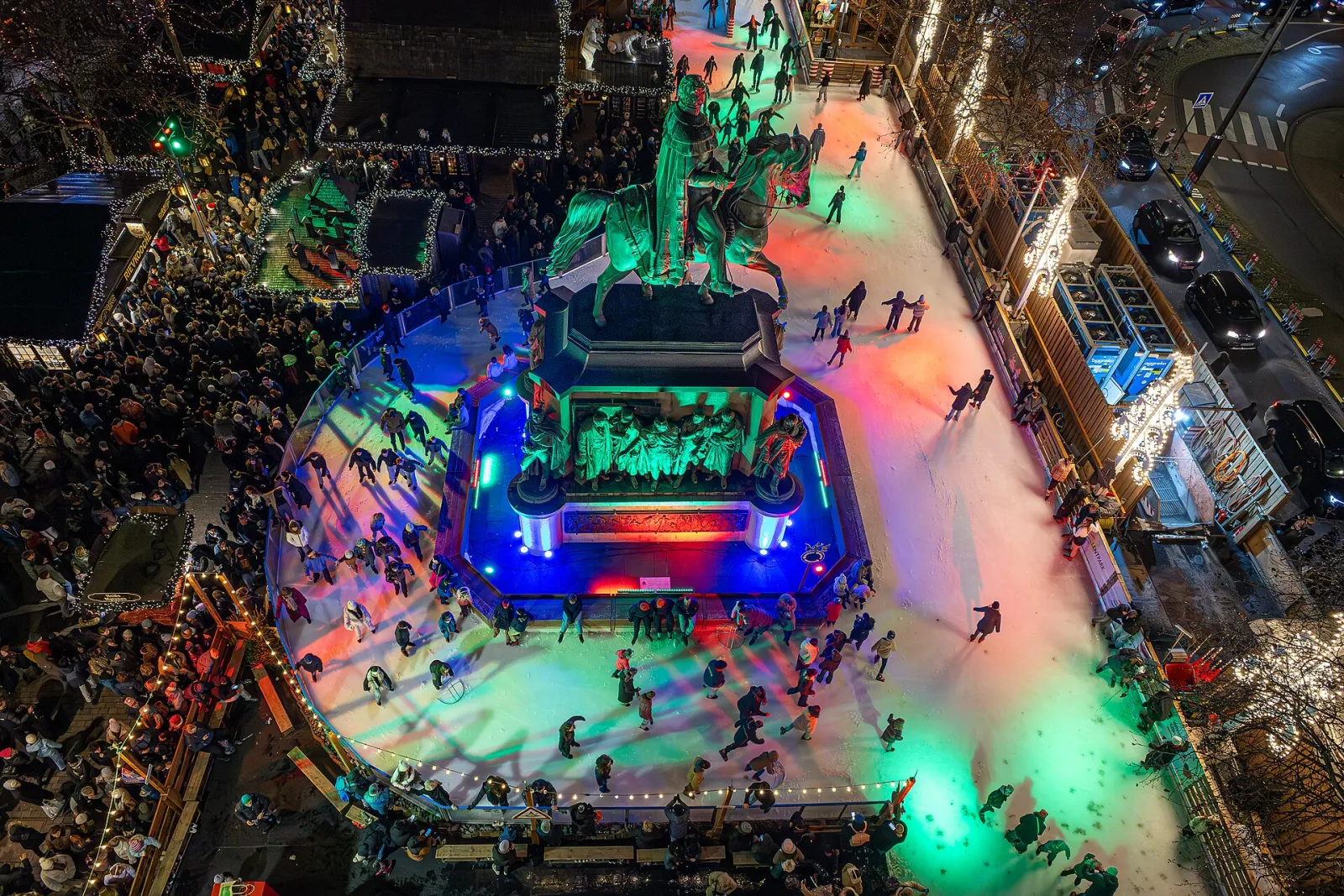 The Heumarkt rink in Cologne from above, lit in colour around the equestrian statue. — Heinzels Wintermärchen Eisbahn