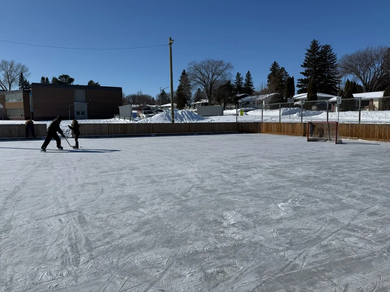 Henry Kelsey School outdoor rink, boards and school behind (Hudson Bay Park / Mayfair / Kelsey Woodlawn Community Association) — Henry Kelsey School Outdoor Rink (Hudson Bay Park / Mayfair)