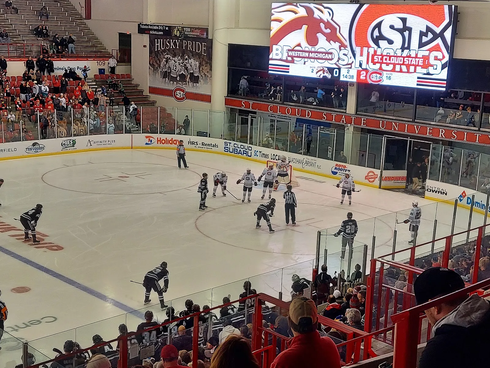 A Huskies game in the main arena seen from the stands, with the video board and 'Husky Pride' banners above the far end. — Herb Brooks National Hockey Center