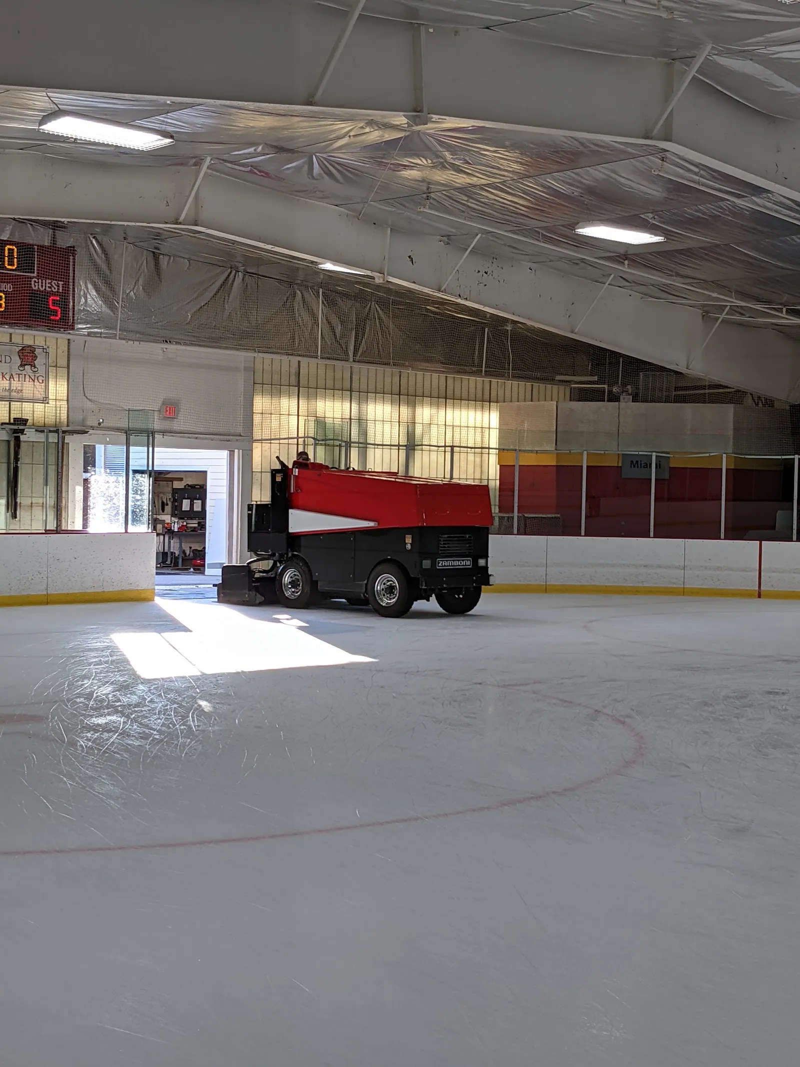 The ice at Herbert Wells Ice Rink with the resurfacer parked by the open rink door, under the lined steel roof — Herbert Wells Ice Rink