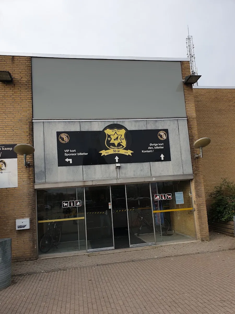 The brick front of Herlev Skøjtehal, with the club crest and ticket signs above the glass entrance doors. — Herlev Skøjtehal