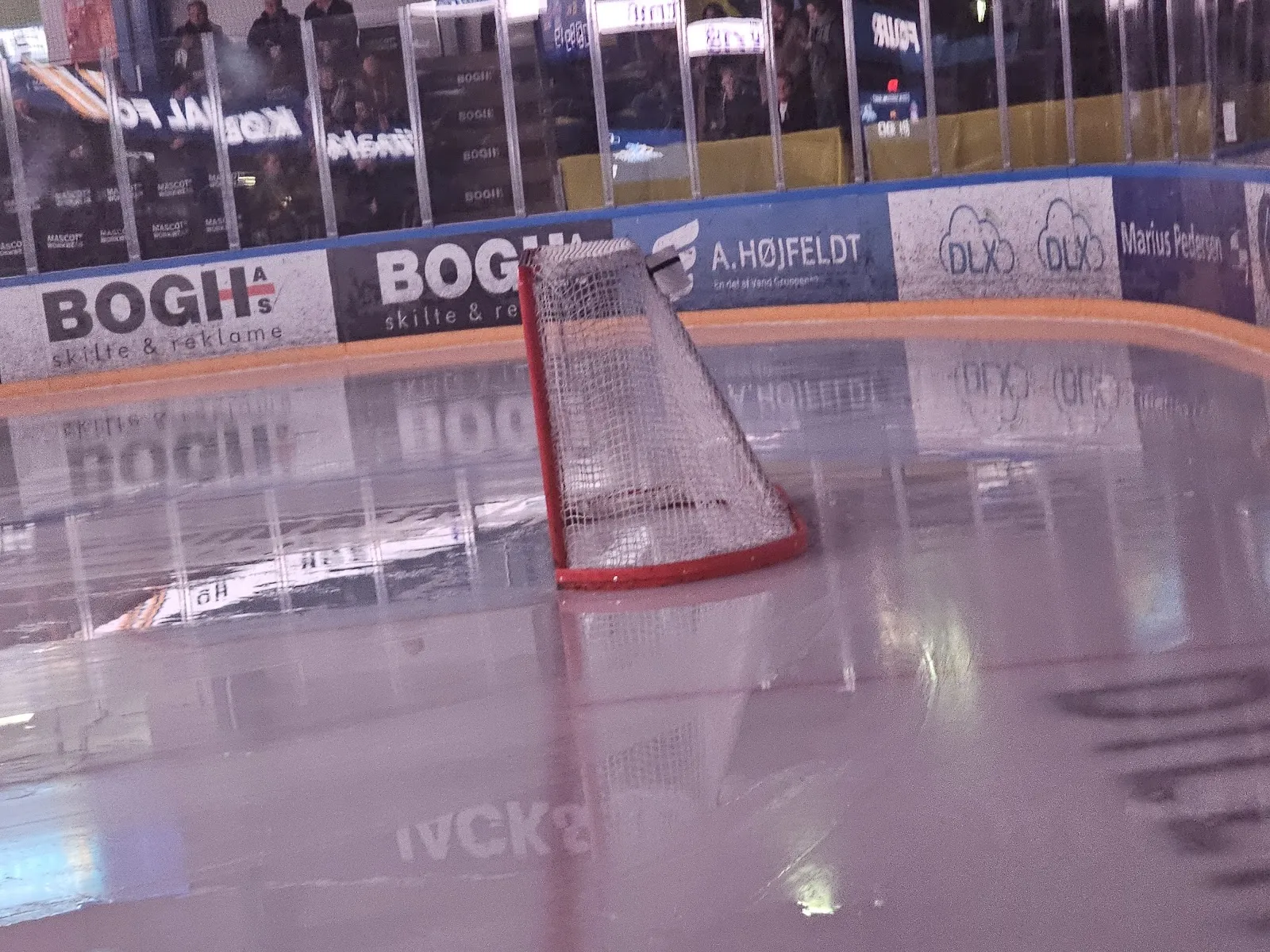 Den tomme is i Herning Isstadion (Kvik Hockey Arena) set fra isniveau, med et mål på isen og reklamebander og tribunerne bagved — Herning Isstadion