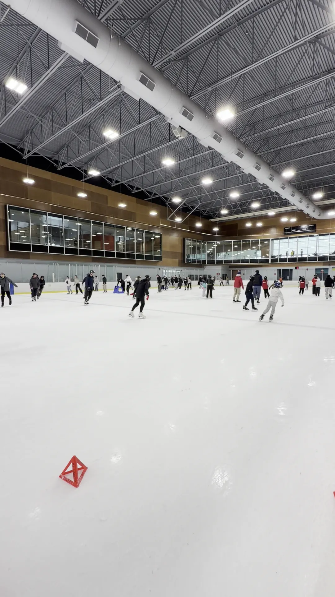 The ice sheet at Hillcrest Rink in a wide view from the boards, under steel roof trusses, with skaters spread across the far side — Hillcrest Rink