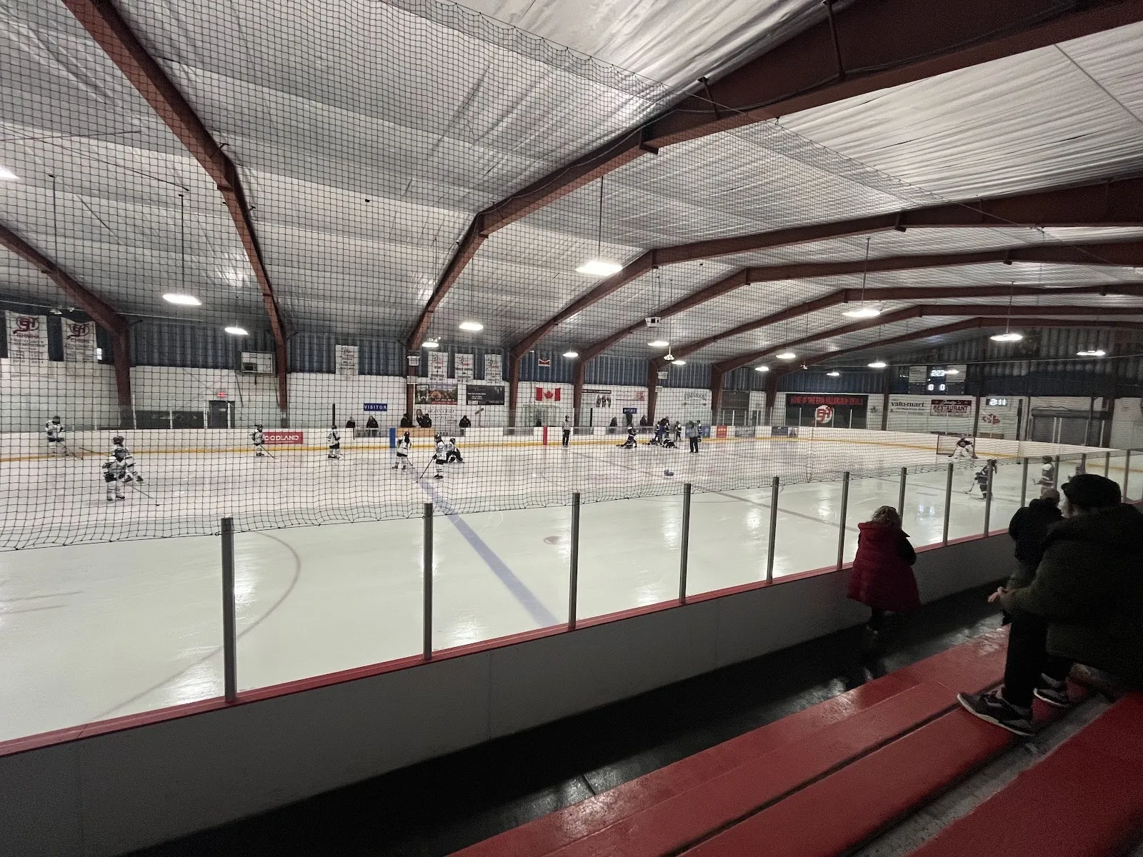The empty sheet seen from the end boards, white ice with a red line under a high arched roof with steel trusses and rows of lights. — Hillsburgh Community Centre