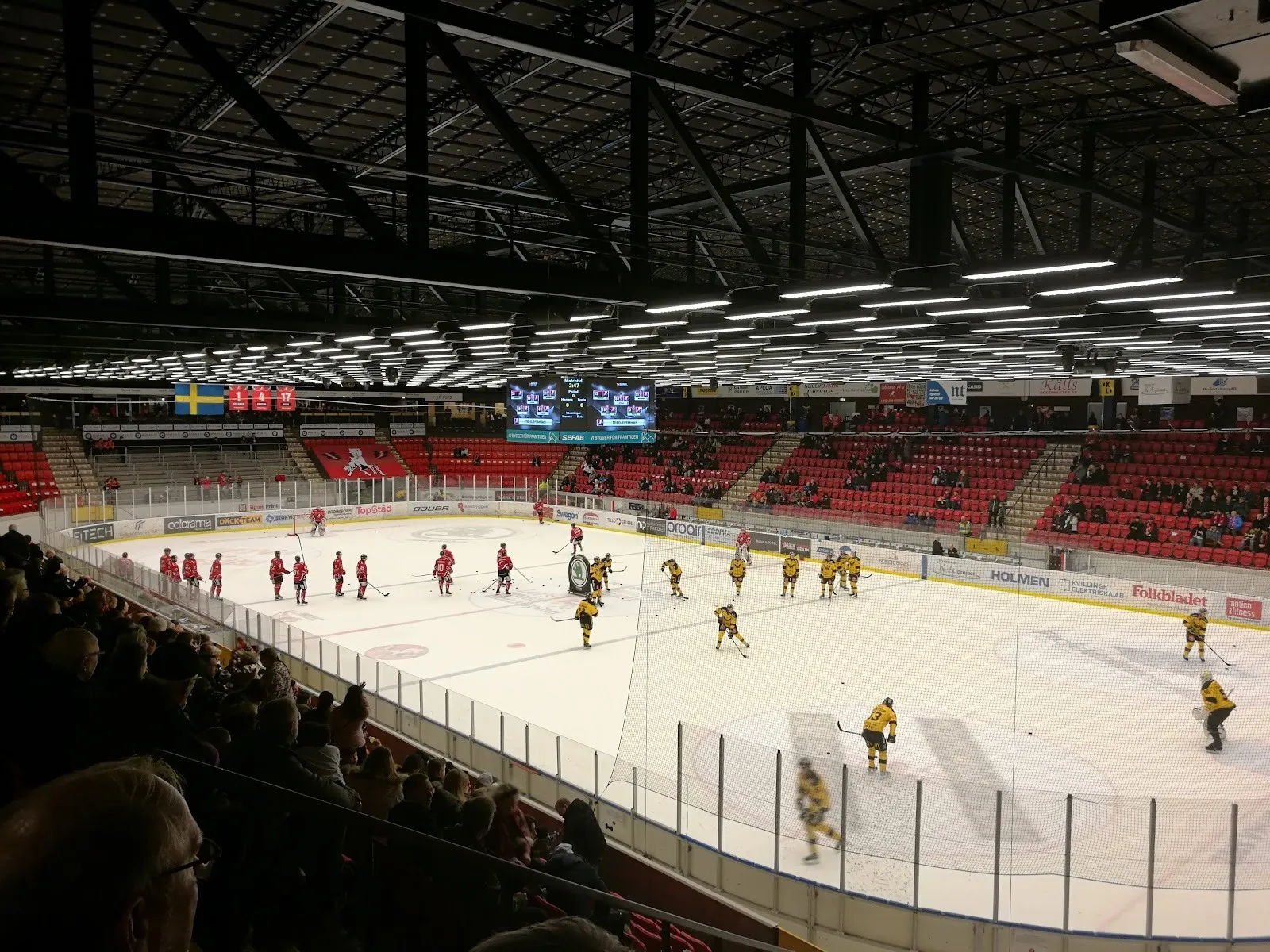 A match in progress at Himmelstalundshallen, players spread across the ice with red seating and a packed stand behind the boards. — Himmelstalundshallen