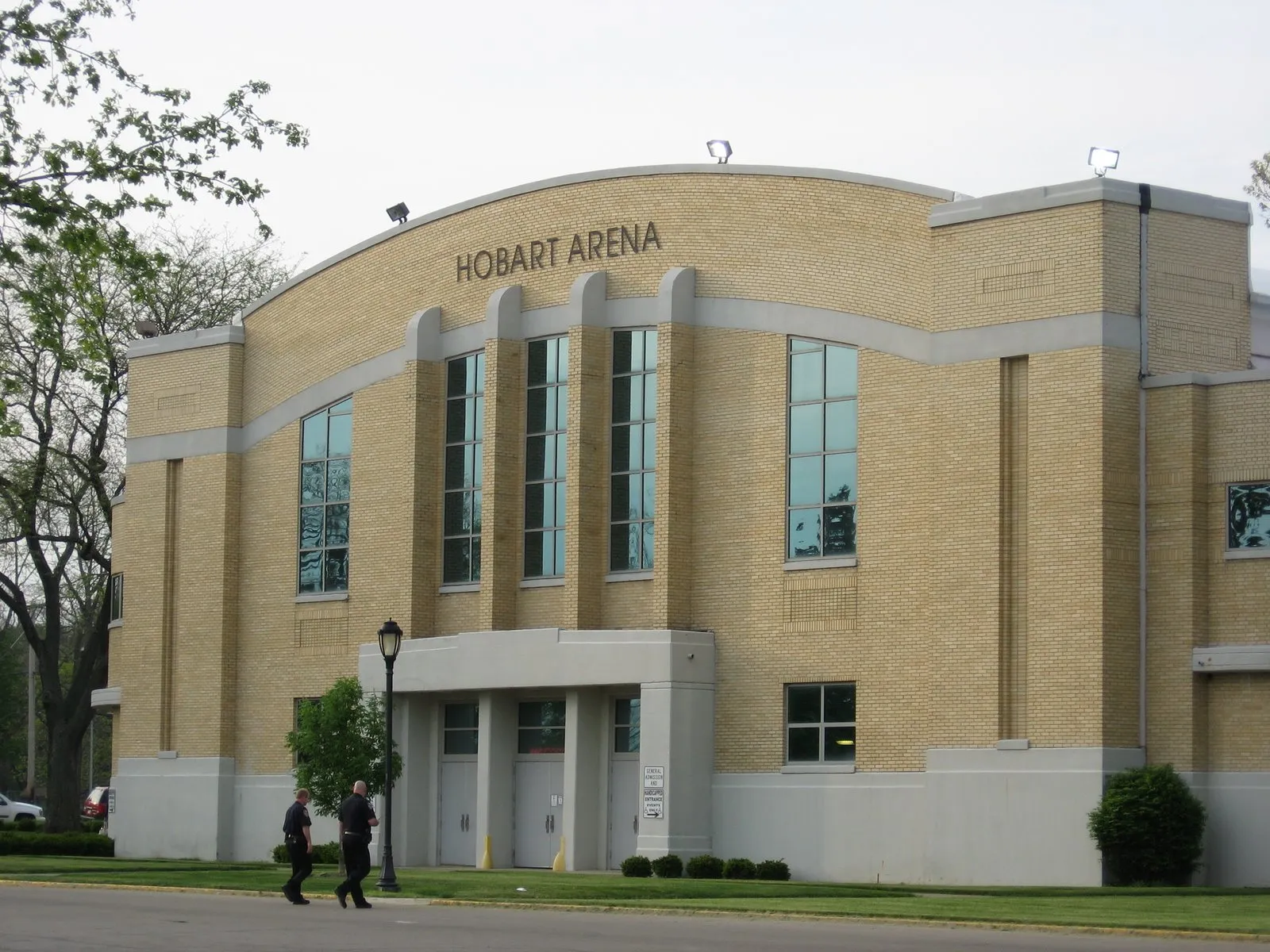 Front of Hobart Arena in Troy, Ohio: yellow-brick facade with a curved parapet bearing the arena's name, tall windows and a covered entrance marked for general admission and handicapped entry. — Hobart Arena