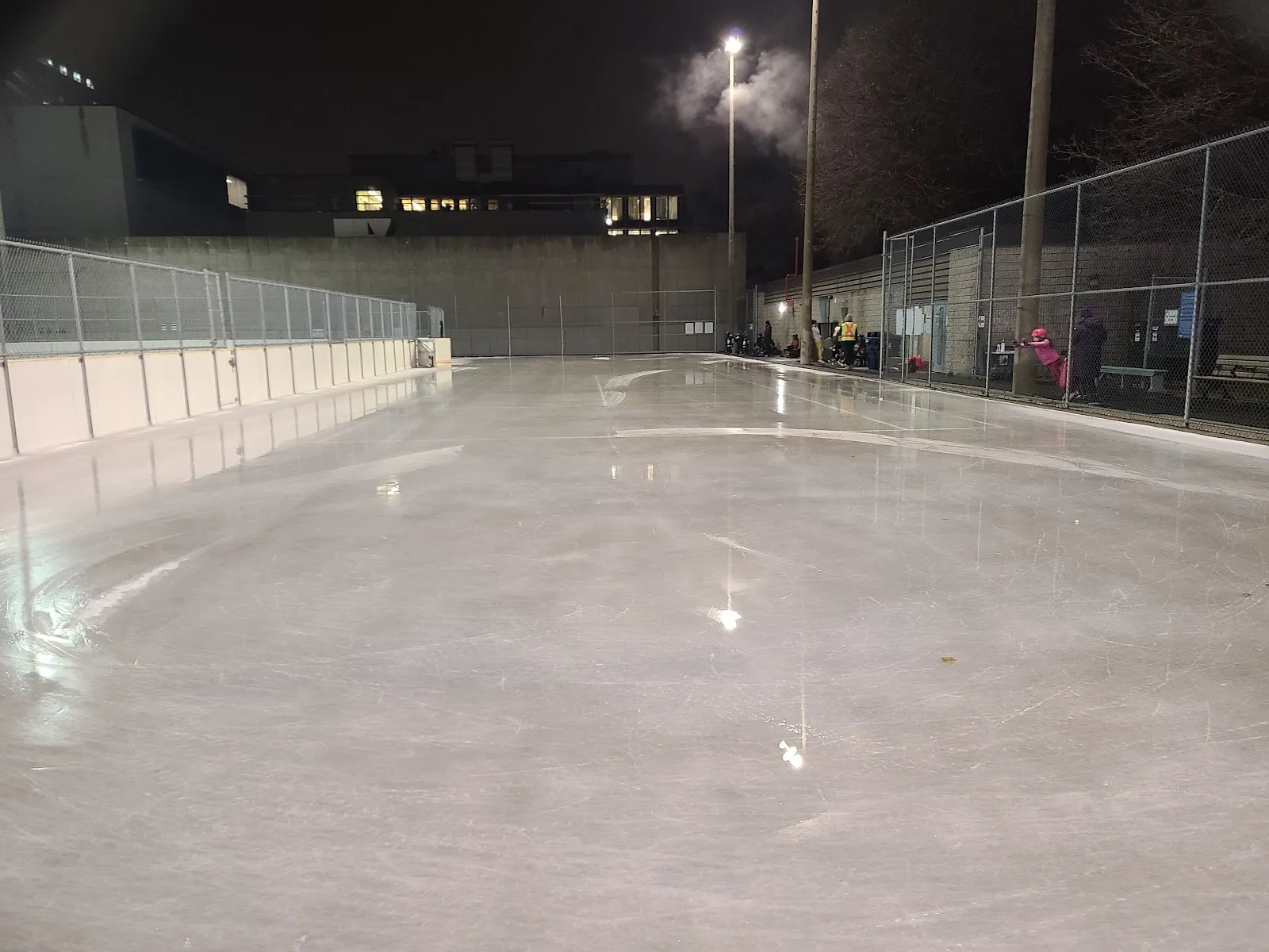 Night view of the Hodgson rink ice and boards along the school wall, lit by floodlights — Hodgson Public School Outdoor Ice Rinks