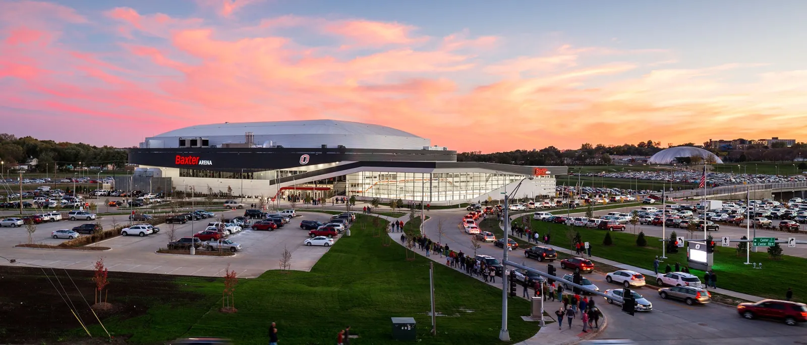 Baxter Arena at dusk with its domed roof and glass entrance, seen across the car park and lawn. — Holland Ice at Baxter Arena