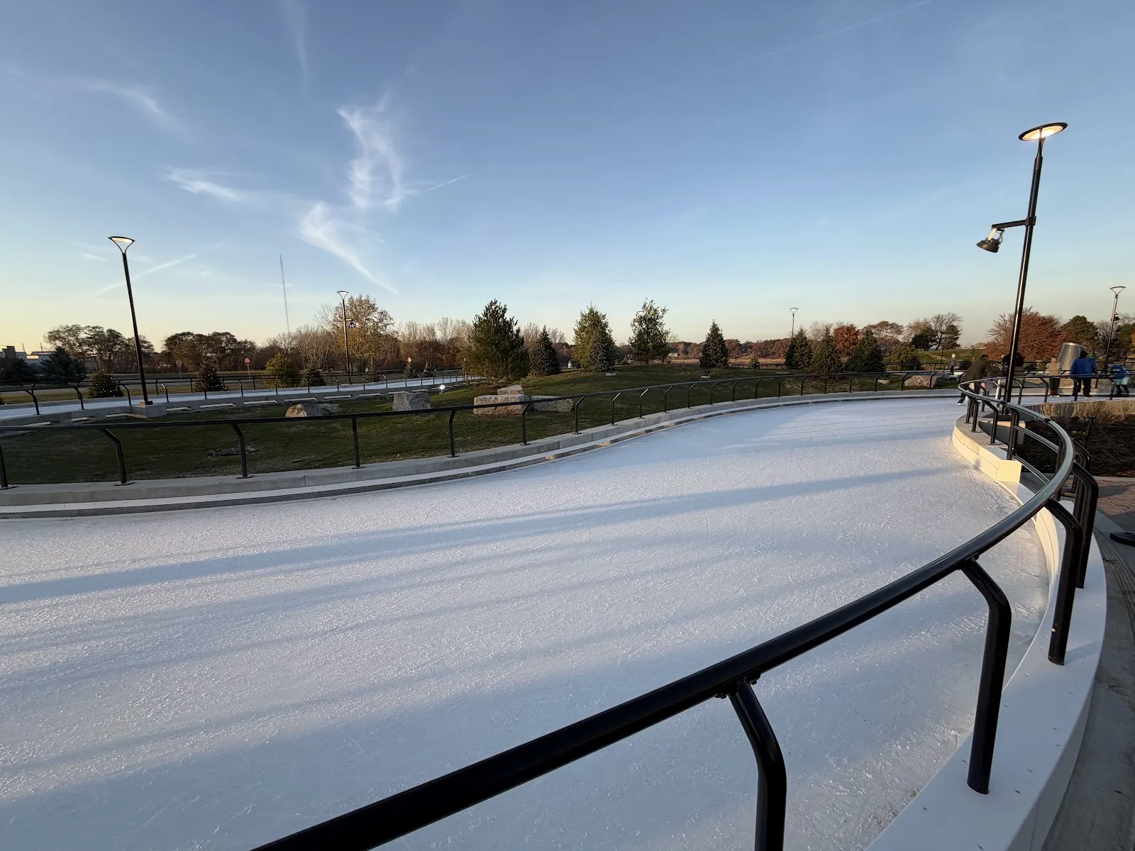 The empty skating ribbon curving past a black rail under a late-afternoon sky. — Holland Ice Park