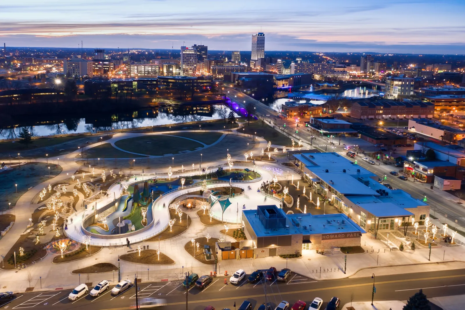 El circuito de hielo y la laguna vistos desde arriba al anochecer, serpenteando por el parque iluminado junto a los edificios de patinaje. — Howard Park Ice Trail