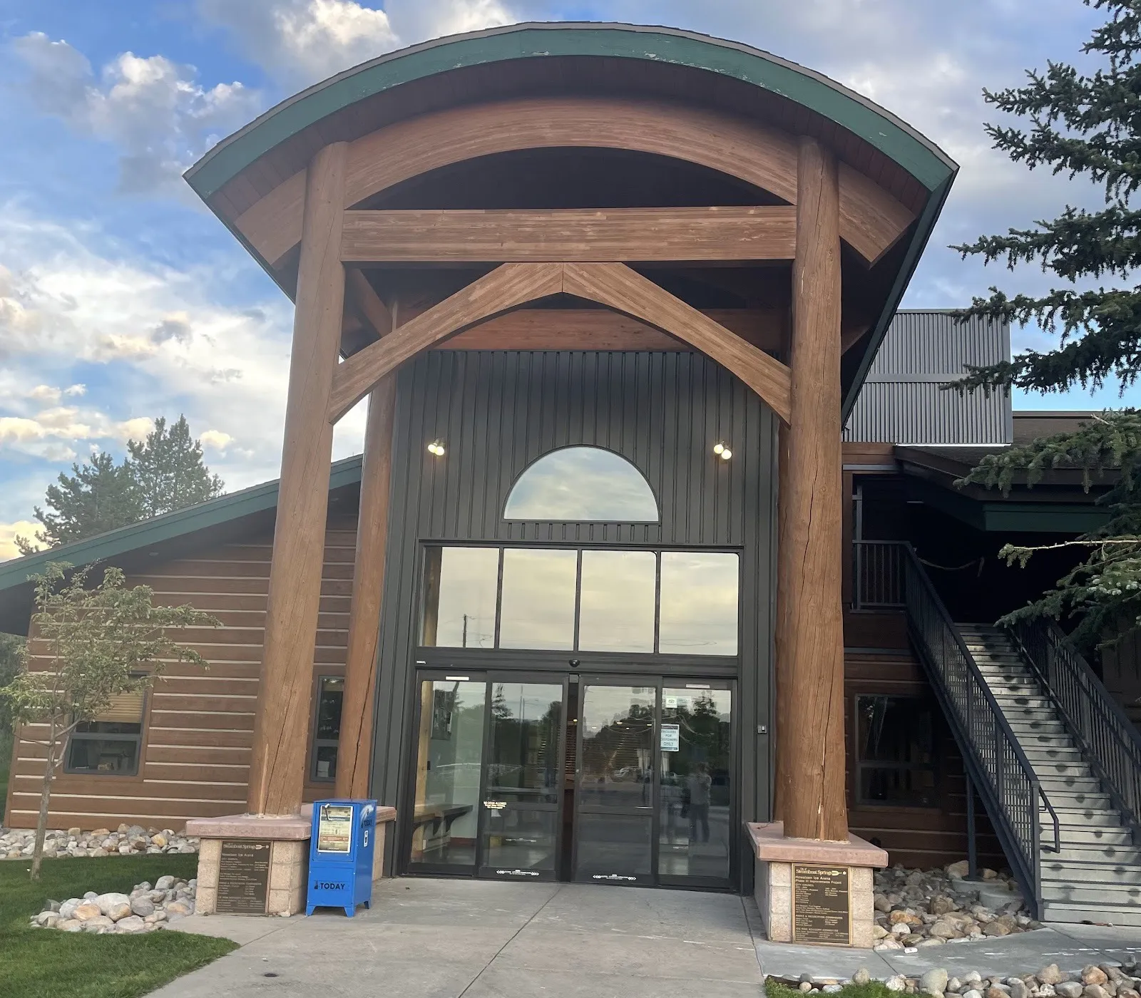 The Howelsen Ice Arena entrance: a curved timber canopy on log columns over the glass doors, between the log-sided wings — Howelsen Ice Arena