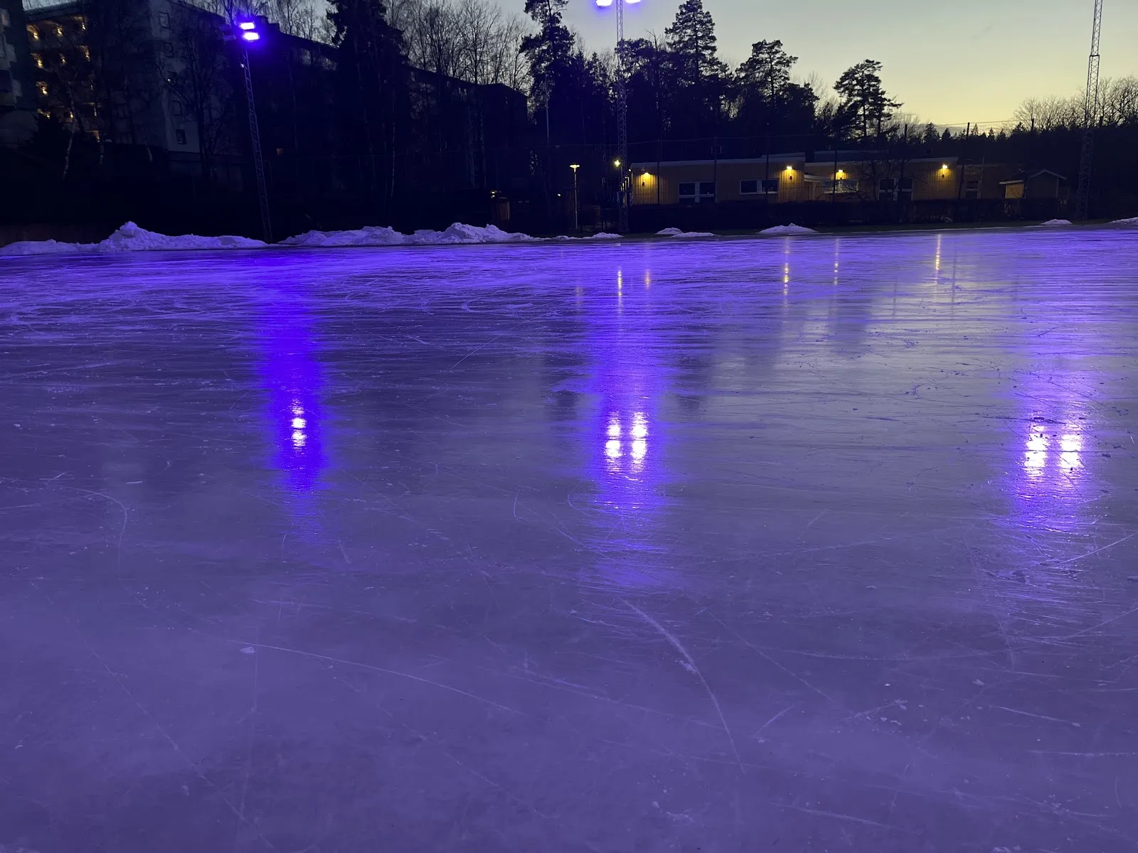 Floodlit outdoor ice at dusk beside Husby ishall — Husby öppna skridskois