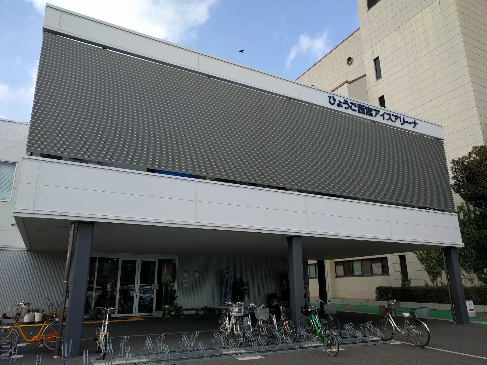 Hyogo Nishinomiya Ice Arenaの建物の正面。上部のファサードにアリーナの名前があり、入口に駐輪場があります — Hyogo Nishinomiya Ice Arena