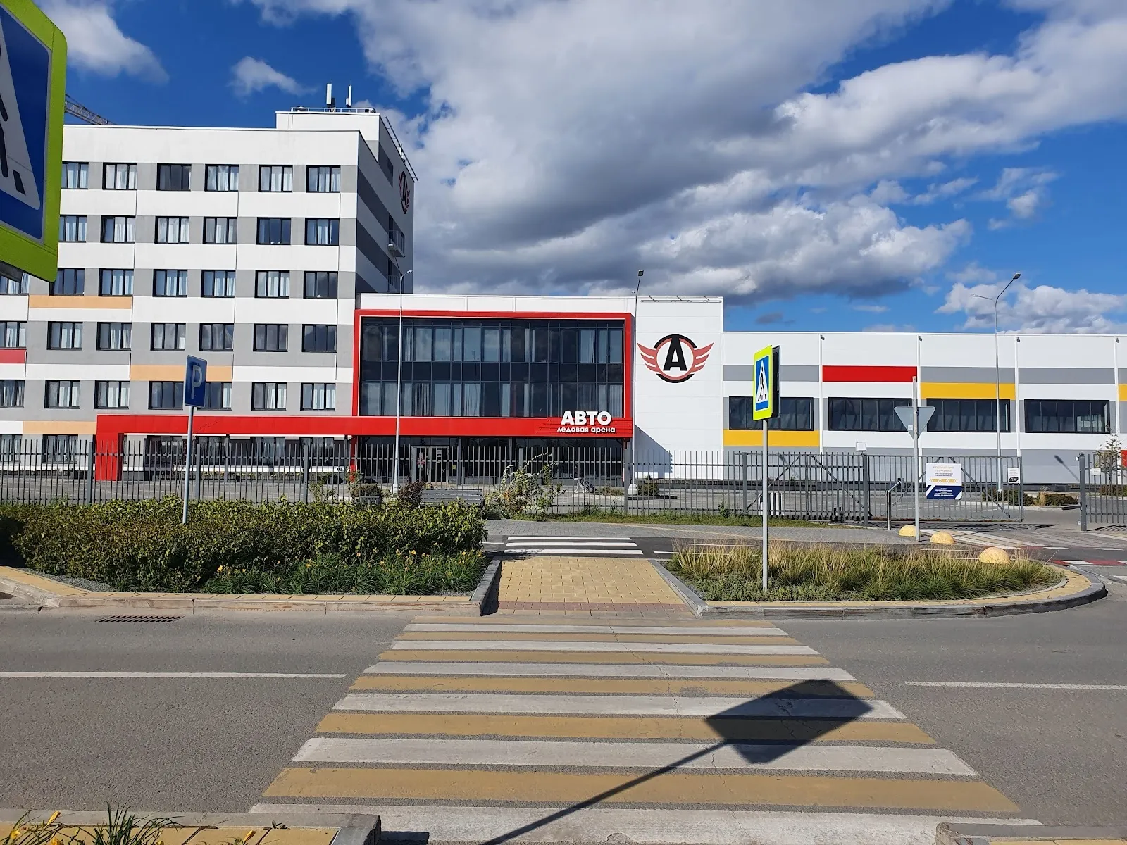 Бело-красный фасад здания ледовой арены «Авто» в Екатеринбурге, вид через пешеходный переход под синим небом. — Ice Arena AVTO