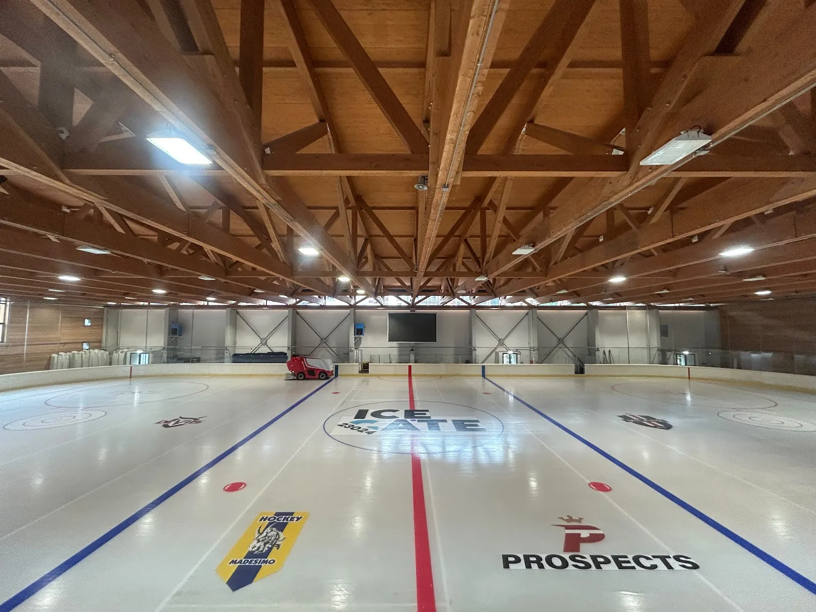 La pista di ghiaccio dell'ICEArena nel Palazzetto dello Sport di Madesimo, con il logo ICE GATE al centro e le travi di legno del tetto sopra. – ICEArena Madesimo