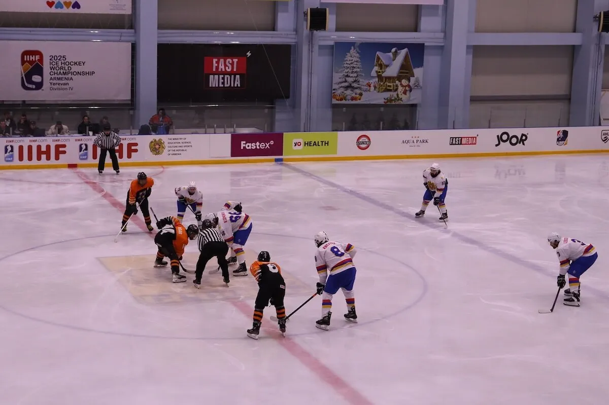 A game on the ice of Ice Arena Yerevan, with the IIHF World Championship boards around the rink and a few spectators behind the glass. — Ice Arena Yerevan