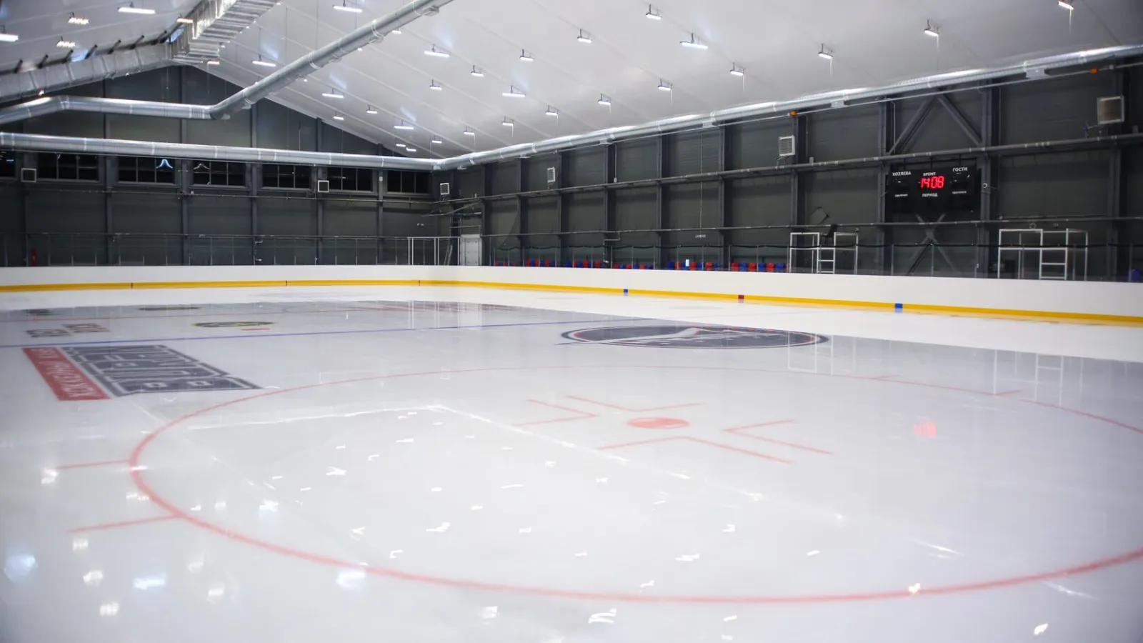 Одно из двух пустых ледовых полей арены Ice Athletics: жёлтая отбойная полоса на бортах, круг вбрасывания и тёмные стены зала — Ice Athletics Arena Moscow