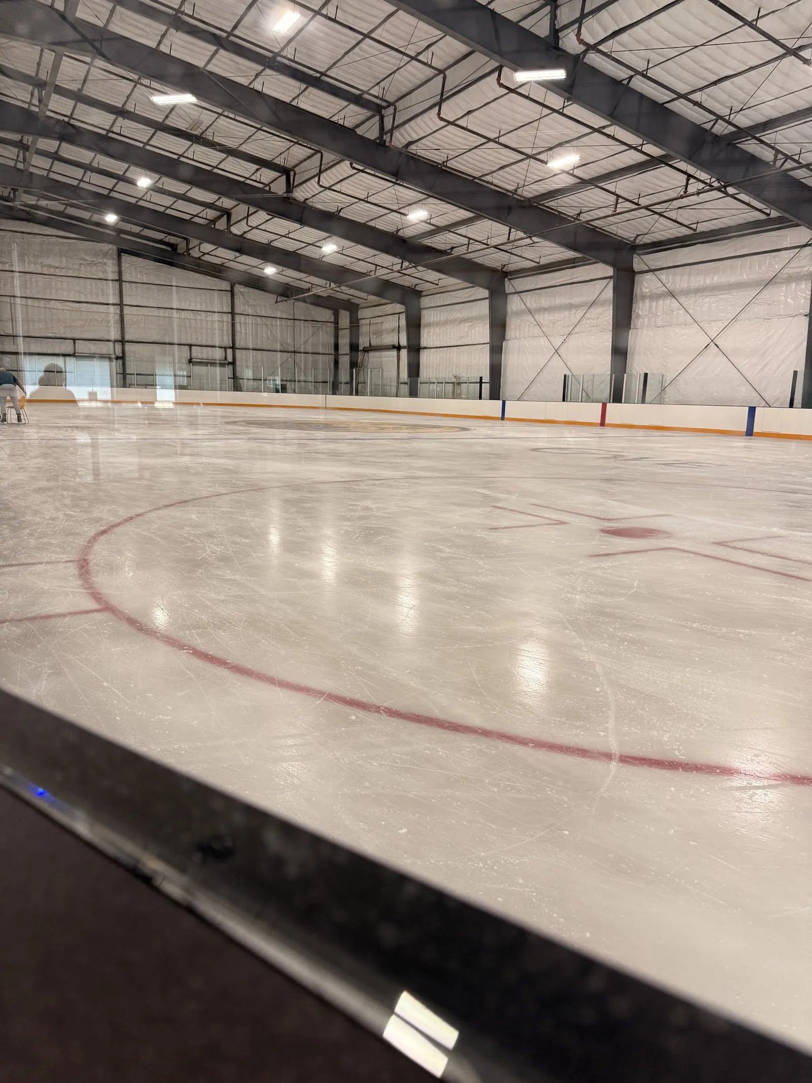 The empty ice sheet under the steel-framed roof, with the boards and face-off circle in the foreground. — The Ice Cave