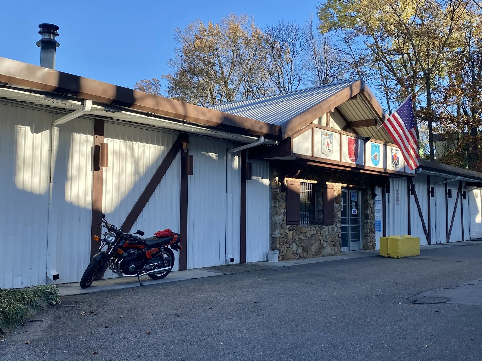 The Ice Chalet's Alpine-style front, a timbered gable with painted crests and a US flag over the stone entrance, under autumn trees. — Ice Chalet