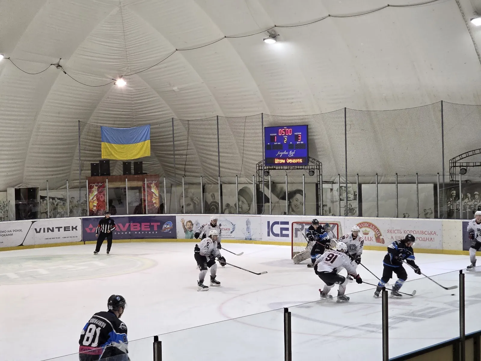 A hockey game on the ice under the white dome of Ice Club, with the scoreboard and a Ukrainian flag at the far end — Ice Club (Vinnytsia)