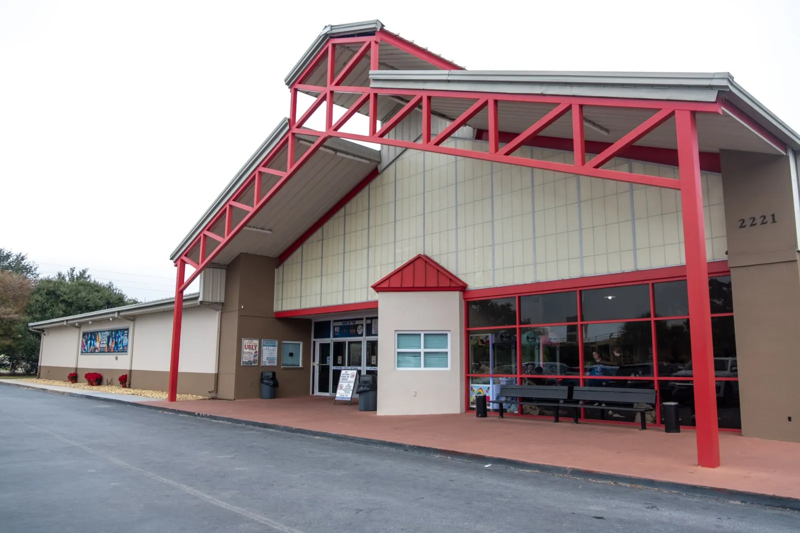 Front of the Ice Factory of Central Florida: a cream-panelled gabled building under a bold red steel truss canopy, with a red-framed glass entrance and a long red-brick forecourt. — The Ice Factory of Central Florida