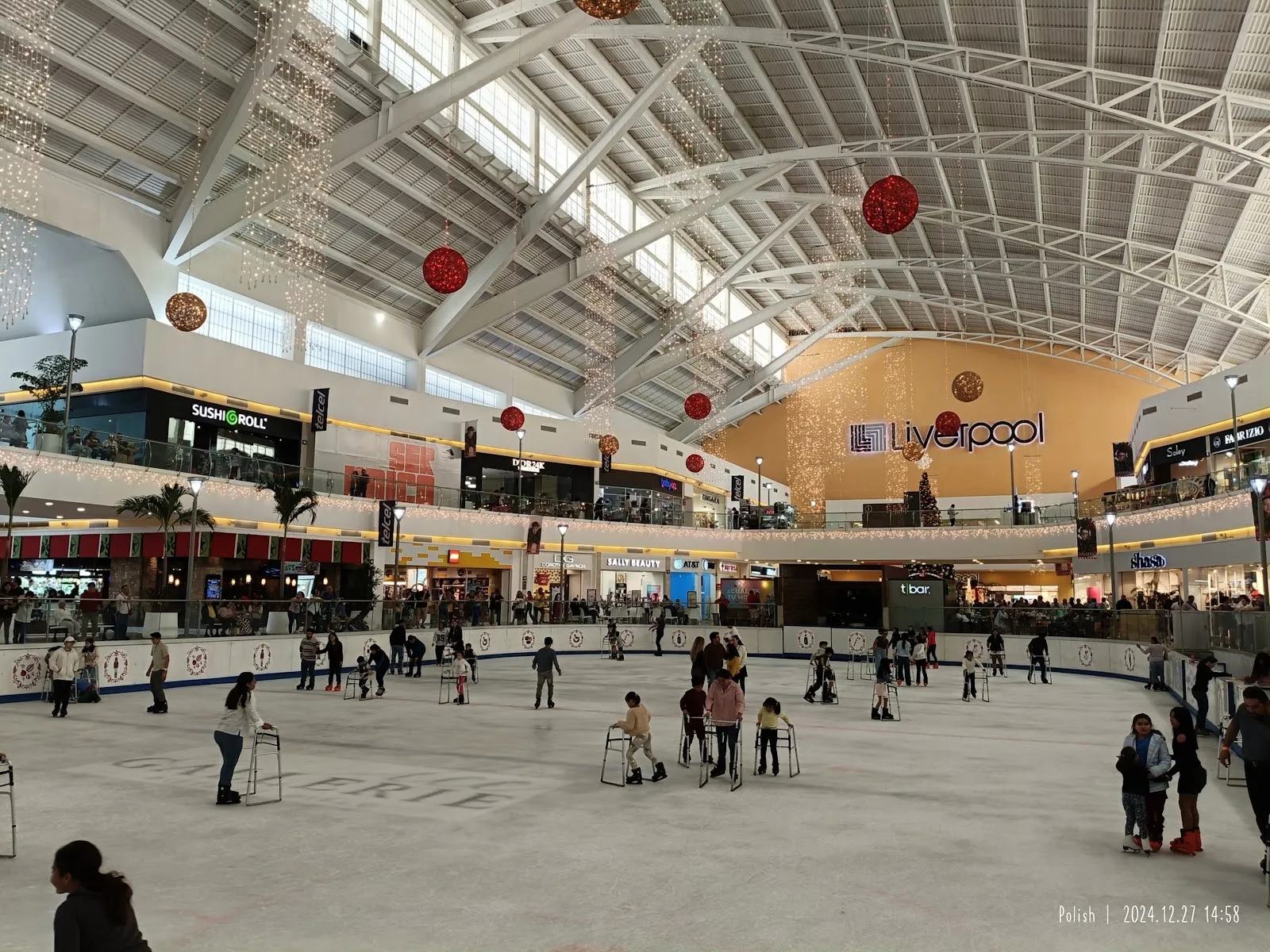 La pista de Ice Gallerie dentro del centro comercial Plaza Galerías en Mérida, con patinadores sobre el hielo bajo el techo blanco arqueado y tiendas alrededor. — Ice Gallerie