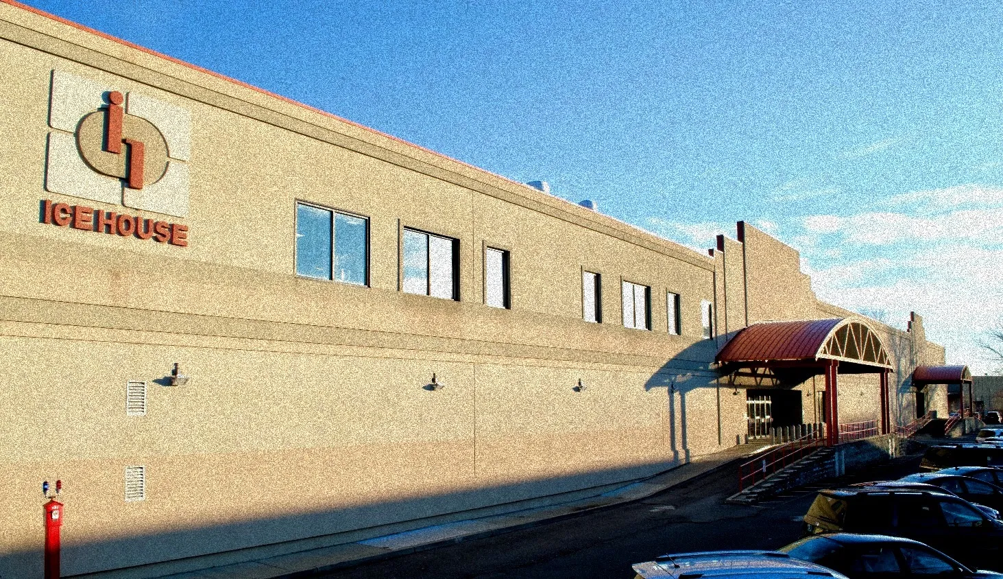 The long tan block building in late-afternoon sun, with the red Ice House logo high on the wall and a curved red entrance canopy over the steps. — Ice House of New Jersey