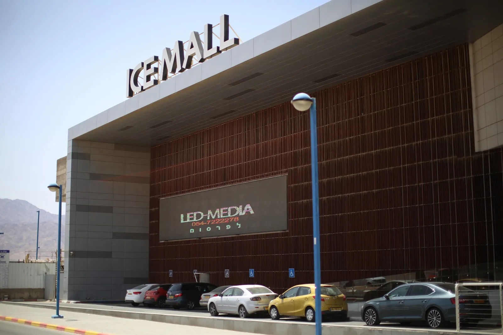 The Ice Mall building in Eilat with its ICE MALL sign over the dark clad wall and the car park below — Ice Mall Eilat