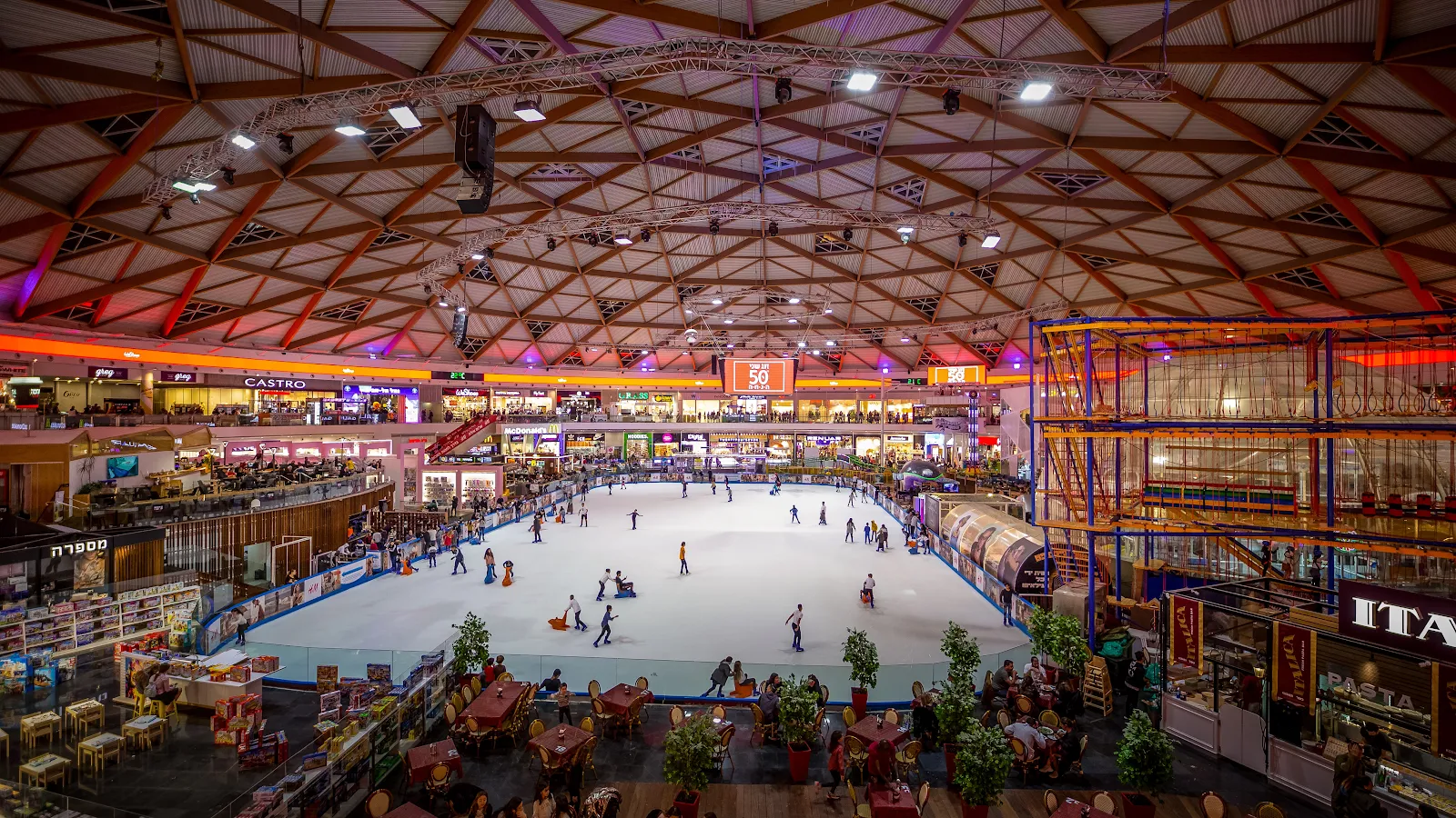 The 1,800 square metre ice sheet at the centre of Ice Mall seen from above, with skaters on the ice under the lattice roof — Ice Mall Eilat